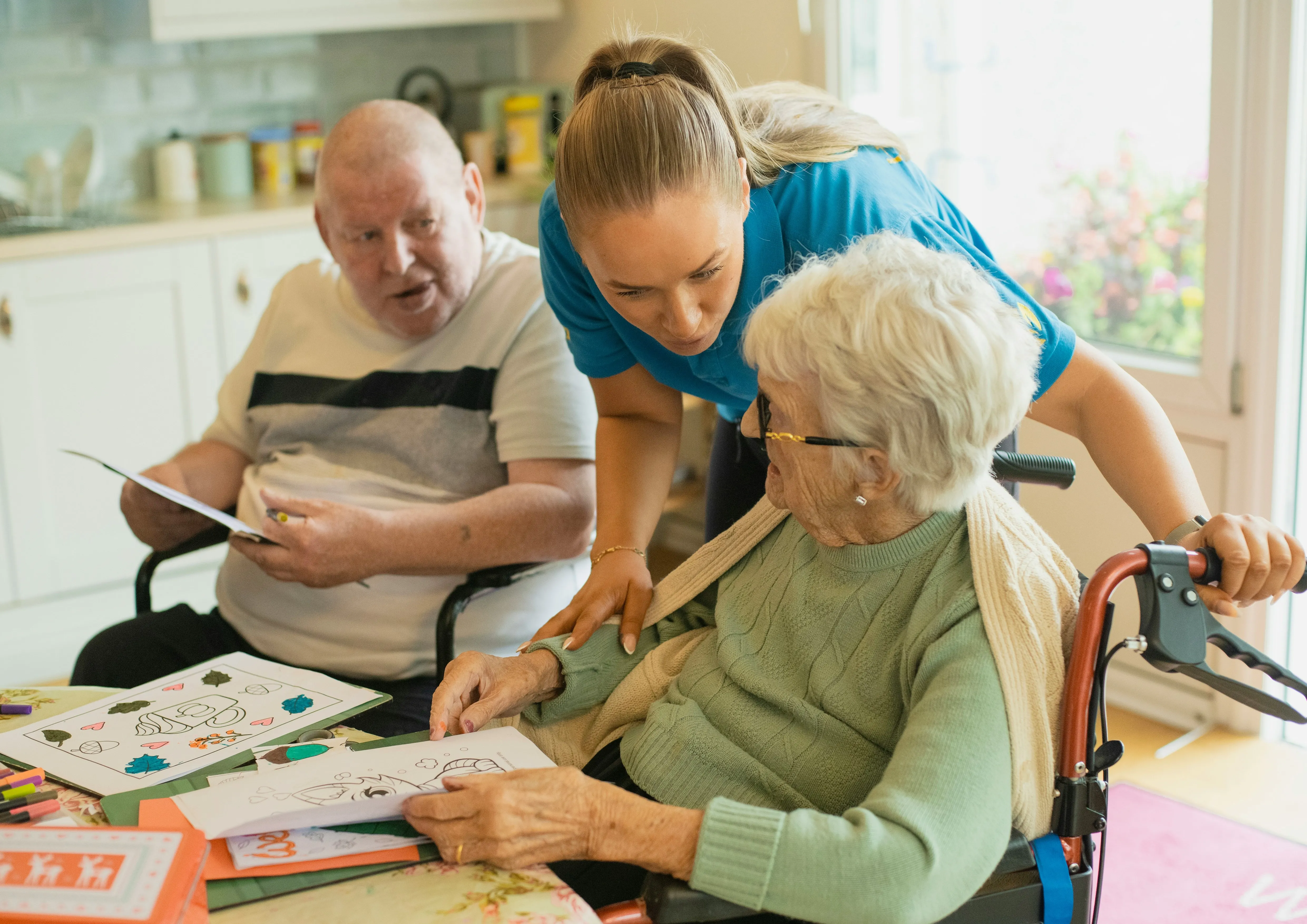 A Pivotal Care carer in navy scrubs sitting alongside an elderly woman, both smiling warmly during a home visit